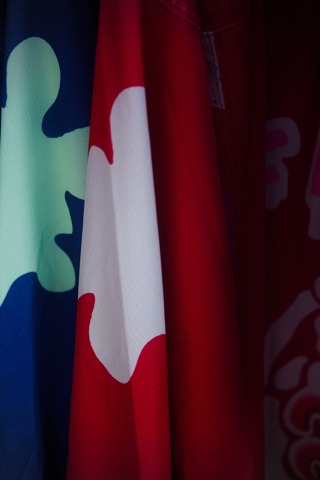 A close-up of a red garment with a large white ink blot motif, partially shown alongside other patterned fabric in blue, green, and pink.