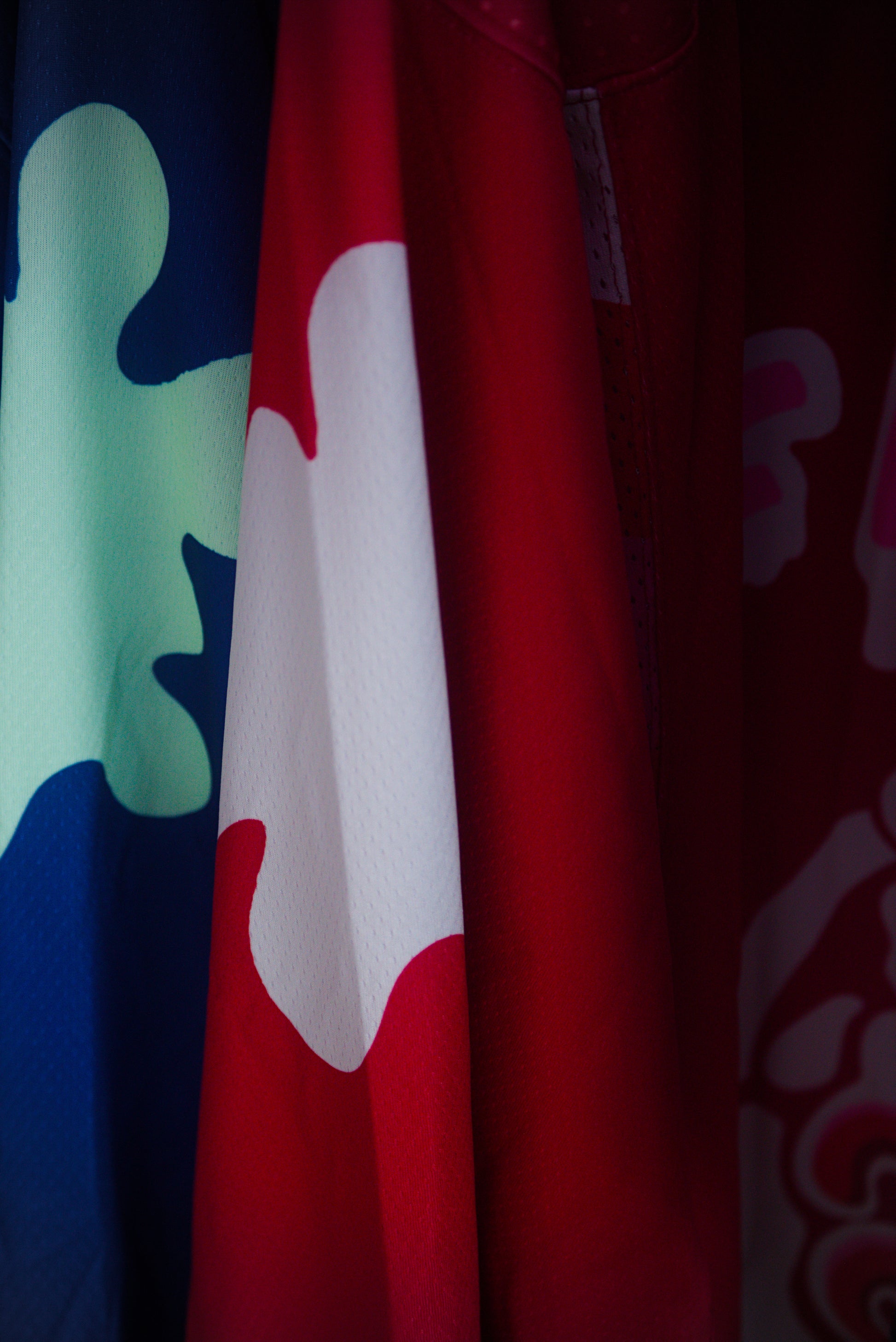 A close-up of a red garment with a large white ink blot motif, partially shown alongside other patterned fabric in blue, green, and pink.