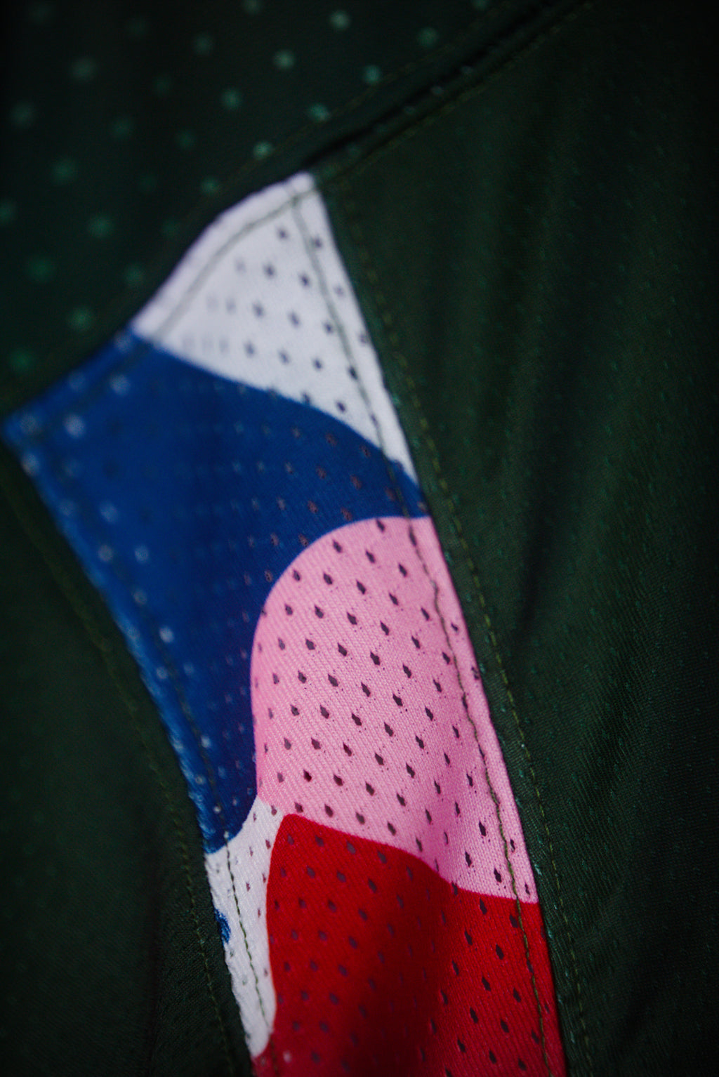 Close-up of a dark green athletic jersey with a colorful mesh panel featuring blue, pink, white, and red sections.